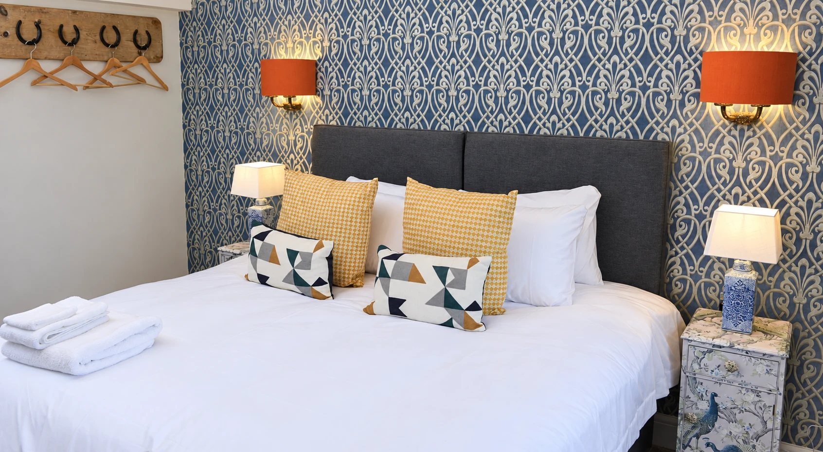 White bedding and mustard cushions against blue patterned wallpaper