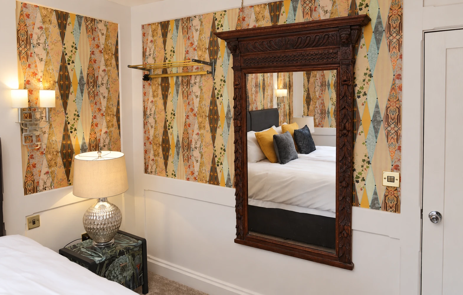 Carved wooden mirror reflecting the bed beside a silver lamp