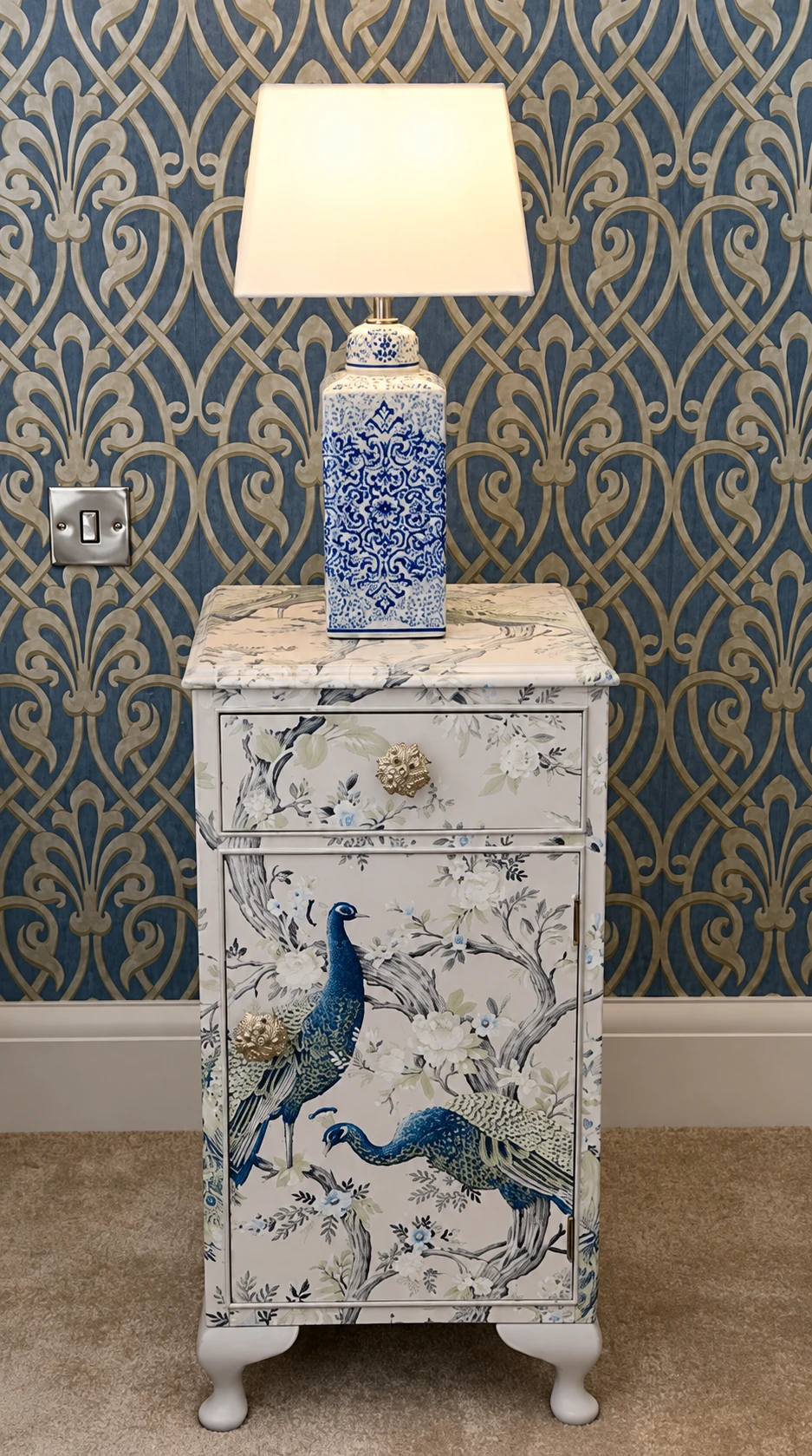 Blue ceramic lamp on a peacock-patterned bedside cabinet