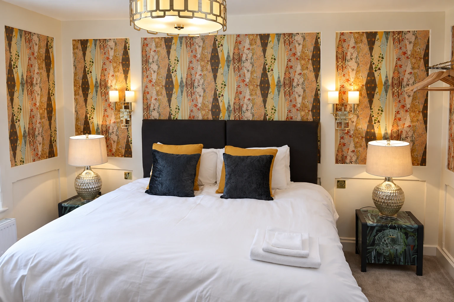 Bedroom with patterned wall panels, silver lamps and dark cushions